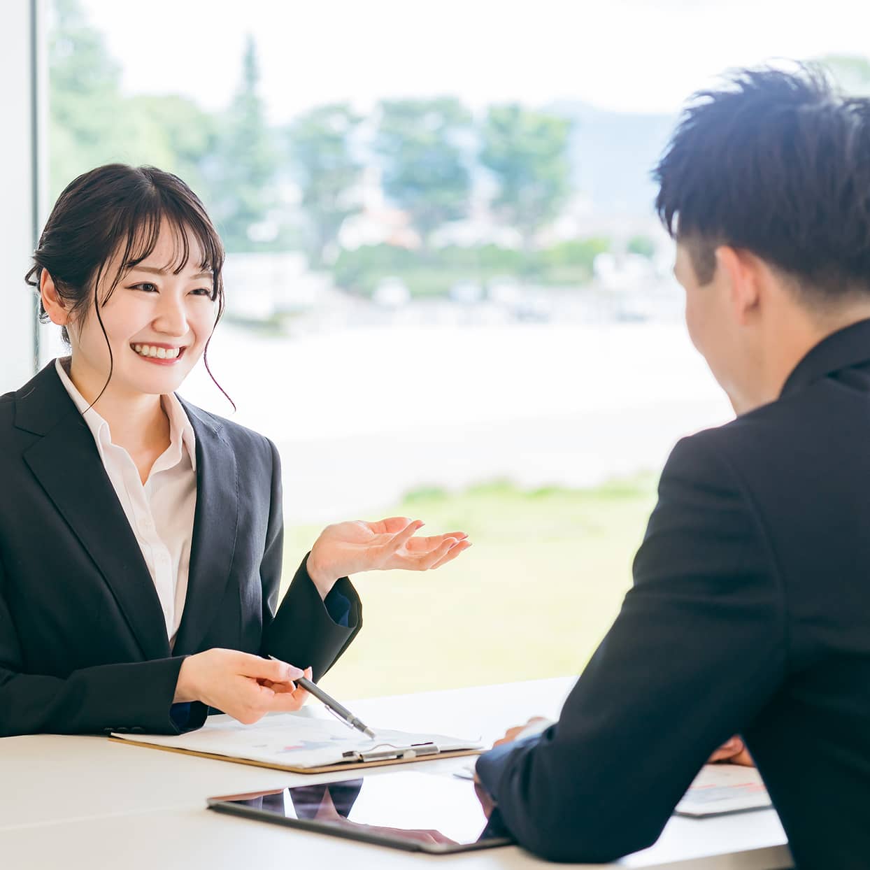 スーツ姿の男女が明るい室内で商談する様子